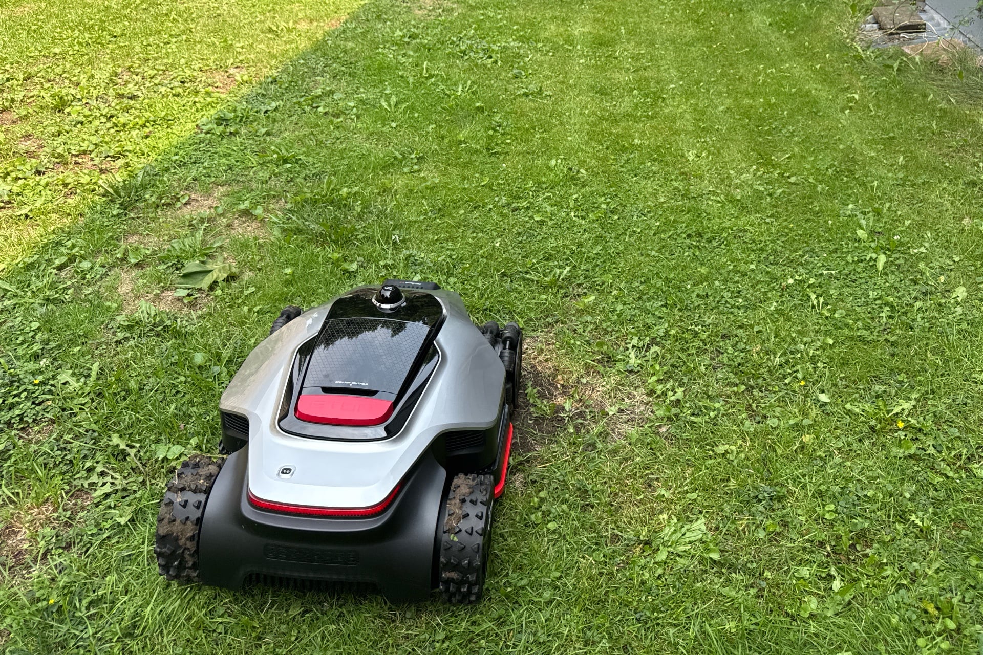 Dreame A3 Awd Pro 3500 photographed in front of a stretch of lawn its mowing. Wheel tracks are clearly visible in the grass.