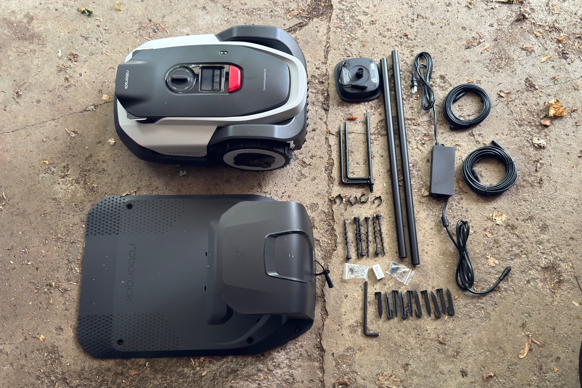 Picture showing the Roborock Rockneo Q110, its dock, and all of the parts that come with it, laid out on a concrete floor.