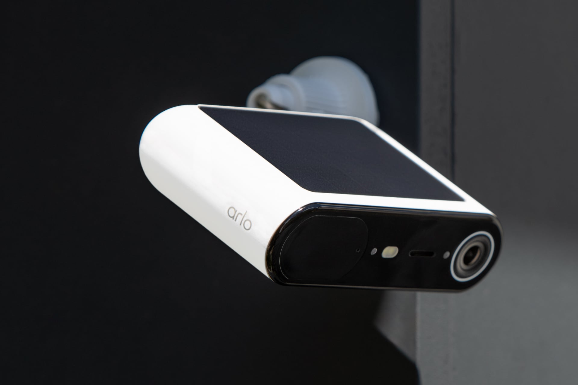 Arlo Essentials Solar in white, pictured close-up with its top, and therefore its black solar panel, visible.