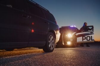 A cop getting out of a police car with a pulled over vehicle