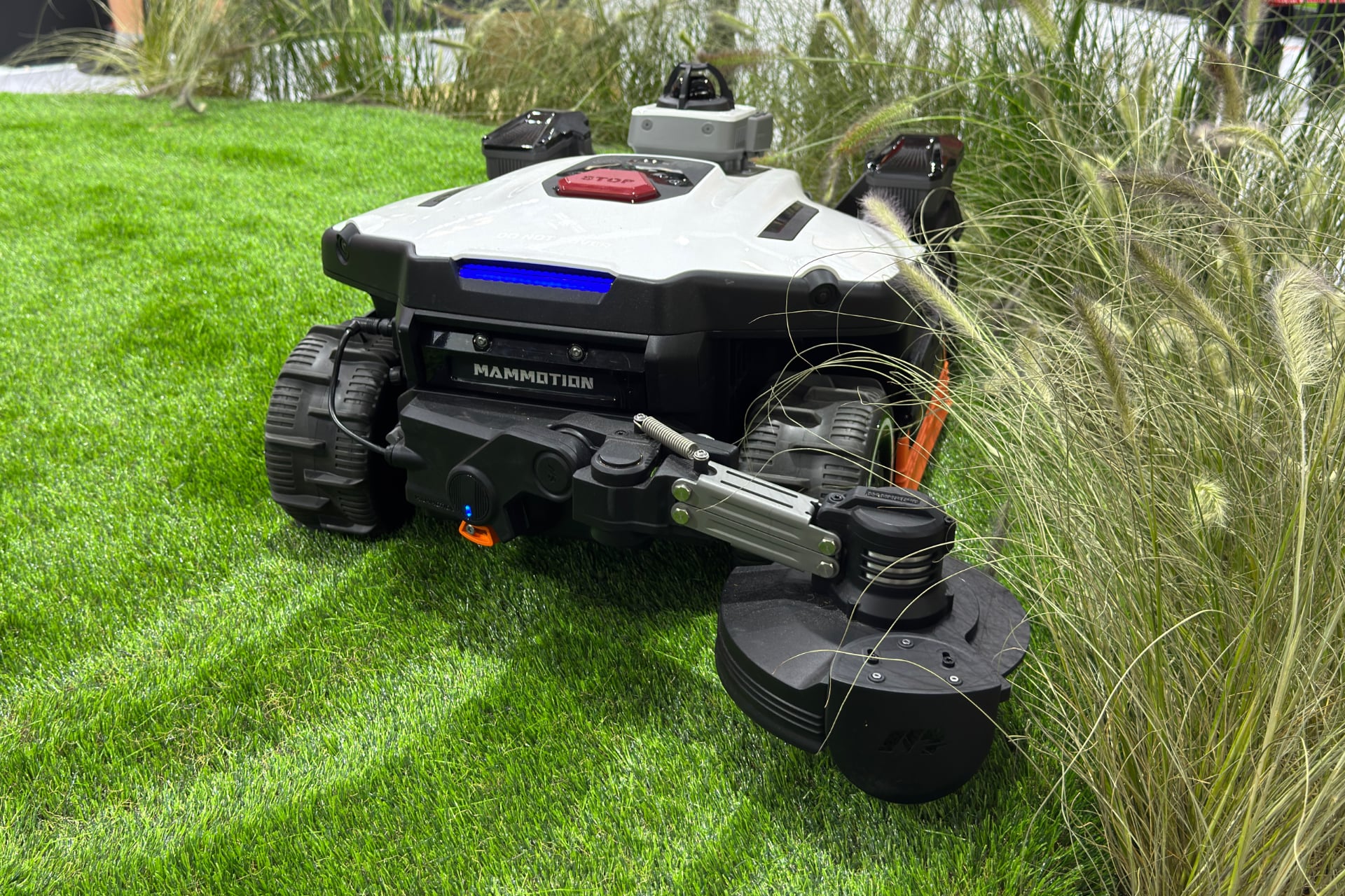 Mammotion Yuba 4 Awd shown from behind with its rear-attached arm reaching to simulate trimming tall grass.