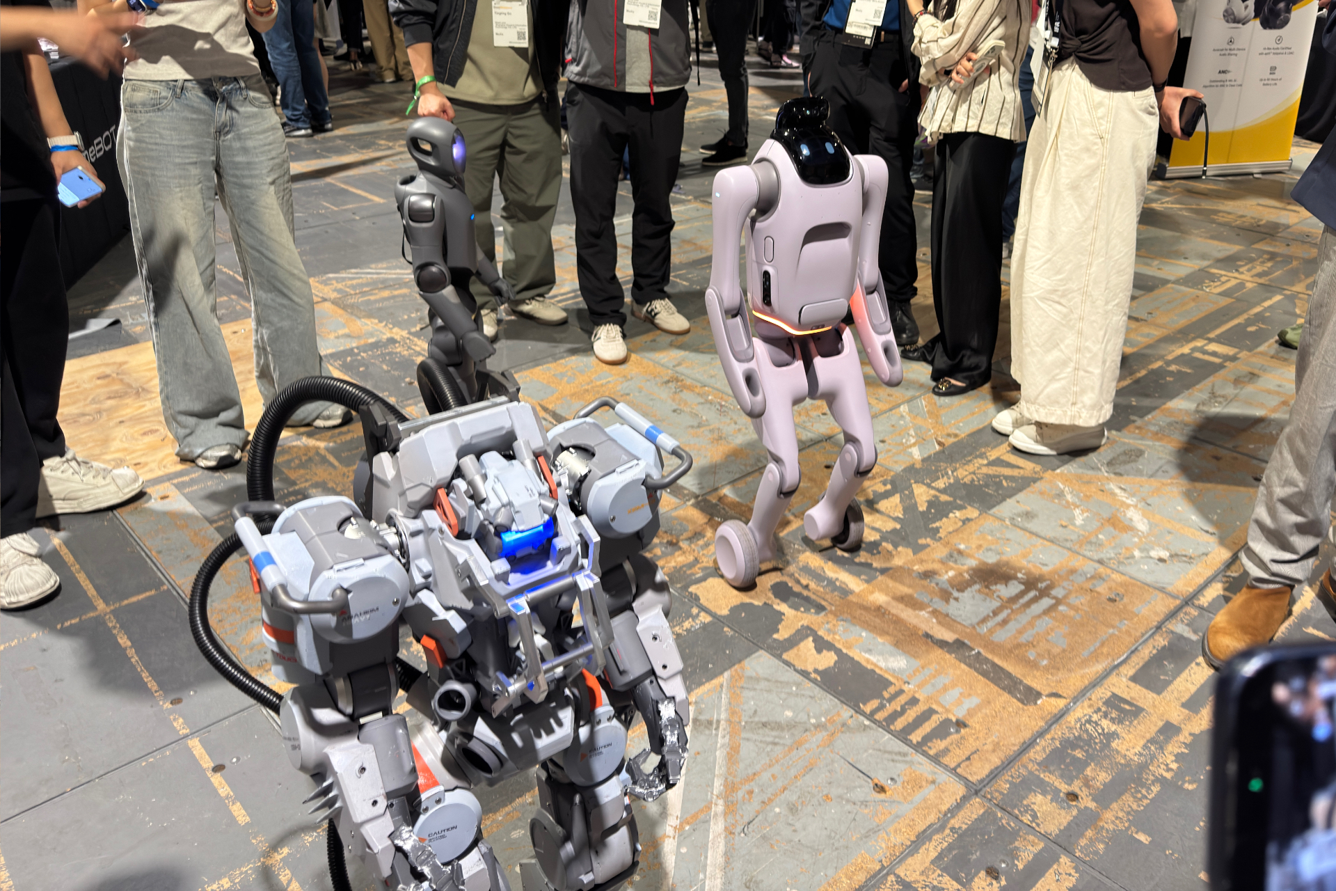 Three robots standing up. One looks like a Robot Jox robot, one is more like a sleek humanoid one, and one has wheels for feet.
