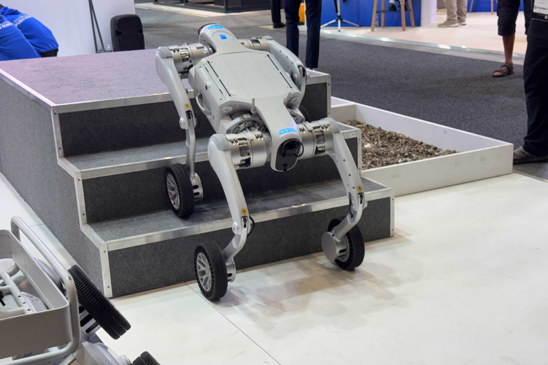 Pudu D5 robot walking up stairs. It's silver, with sensors on the front and back.