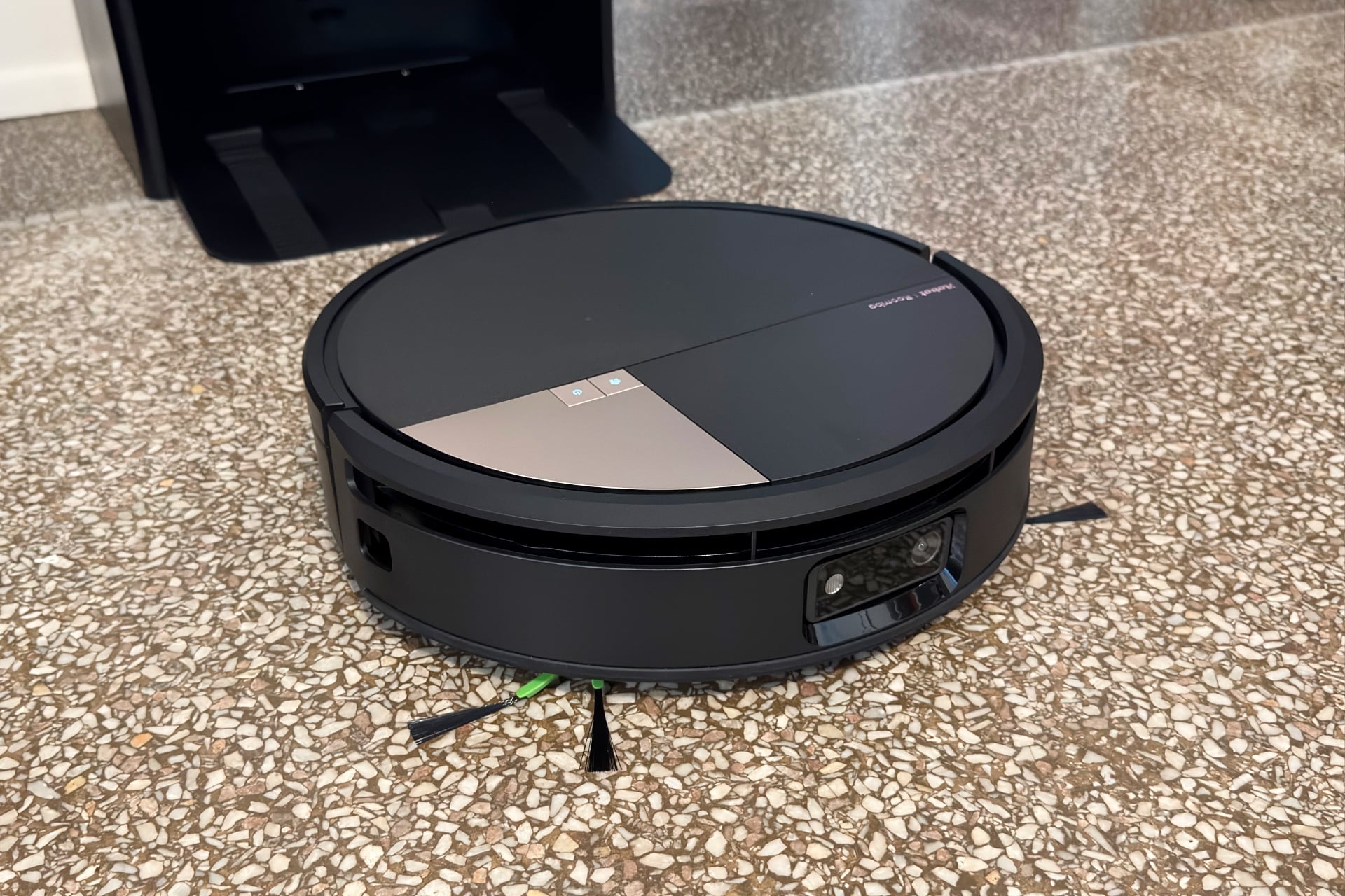 High-angle, three-quarter view of the Roomba Max 775 out of its dock. Its side brushes are visible, poking out from the bottom, as are its LiDAR sensor cutout and front-facing camera.