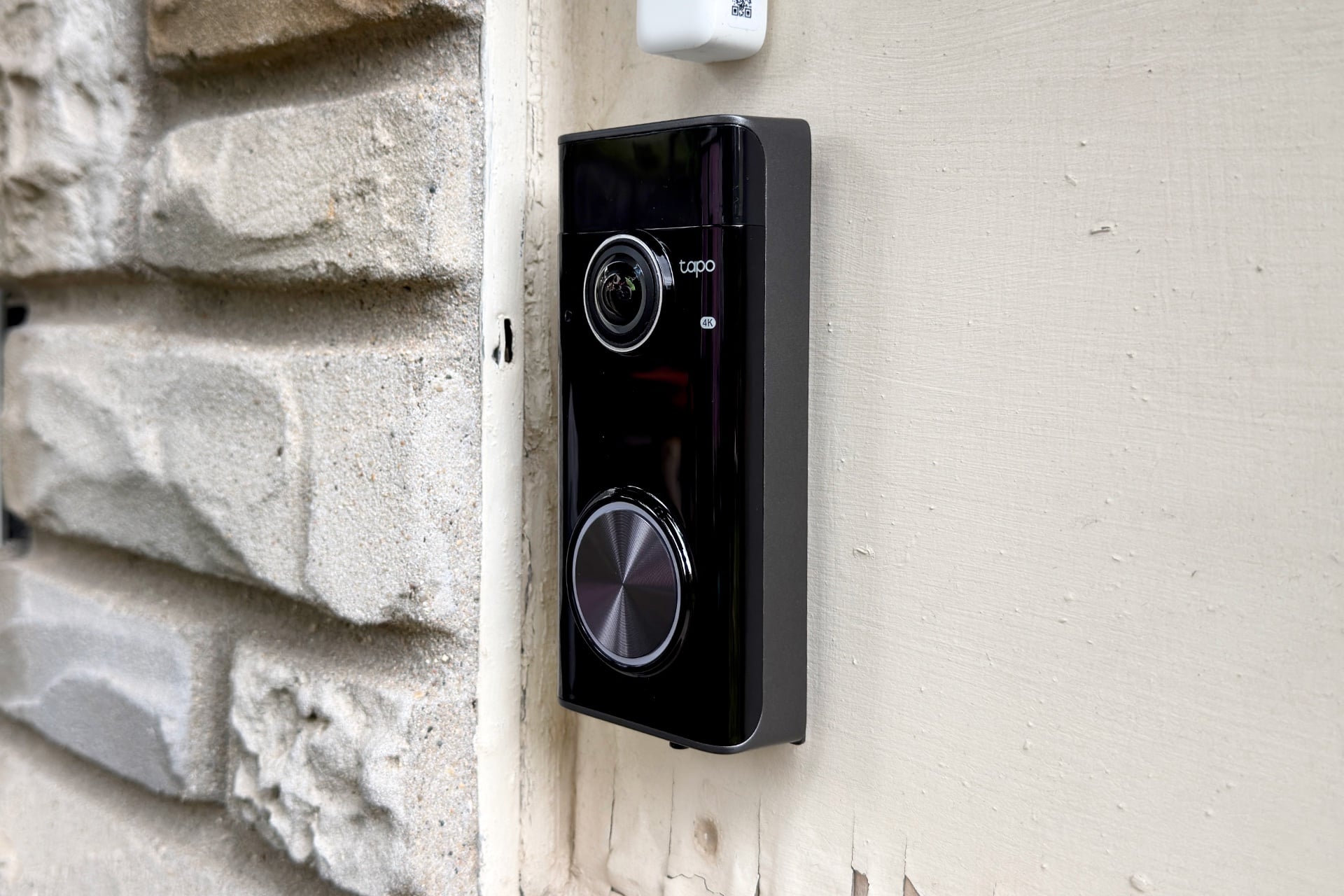Picture of the Tapo Doorbell Pro D260 taken at an angle, showing the glossy, black front, its large doorbell button, and dark gray side.