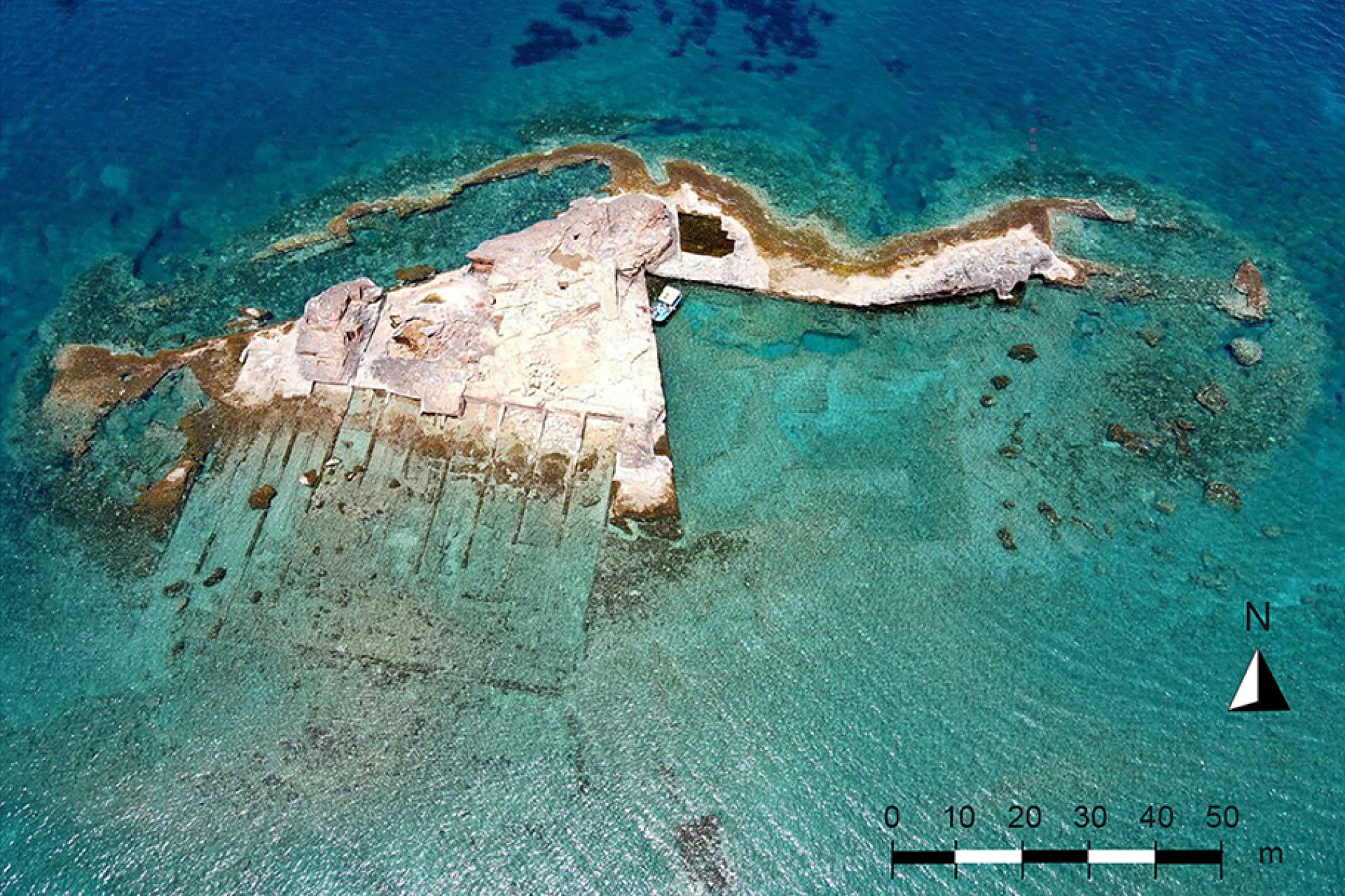 Drone image of Hammam Island along Cyrene showing 40 m-long slipways and extensive removal of bedrock. The submerged rock wall of the wave trap and the broken wall along the northern edge of the island are visible.
