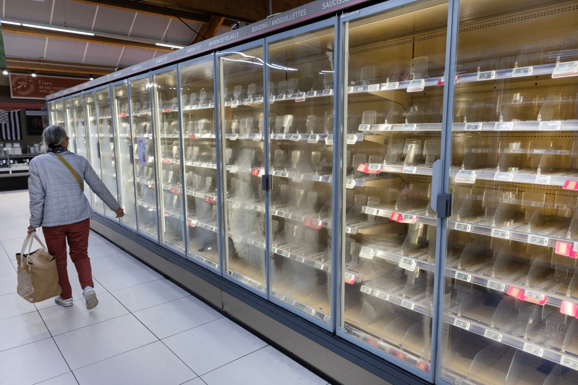 A woman walks past empty fresh-food refrigerators at an Intermarché supermarket in Névez, western France, on October 12, 2026, following a cyberattack affecting the French supermarket chains Intermarché and Cooperative U that caused their refrigerators to defrost.