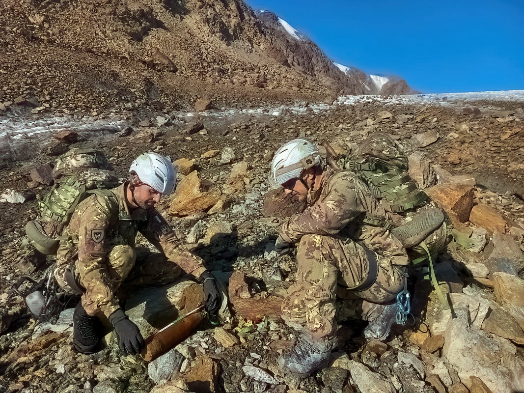 Two Italian army personnel handle a WWI warhead in the rocky landscape of the Dolomites 