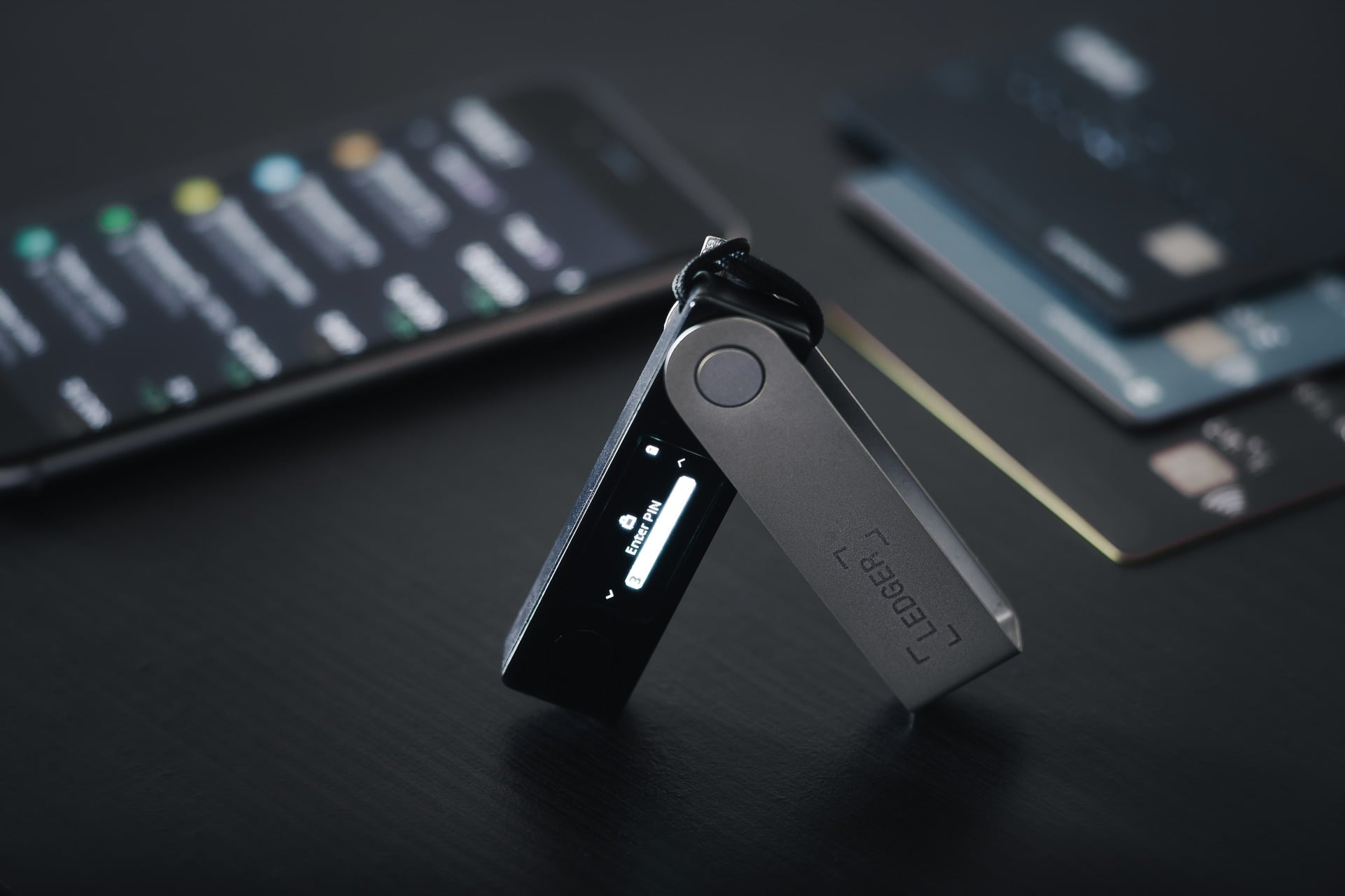 A Ledger hardware wallet next to a smartphone and credit cards