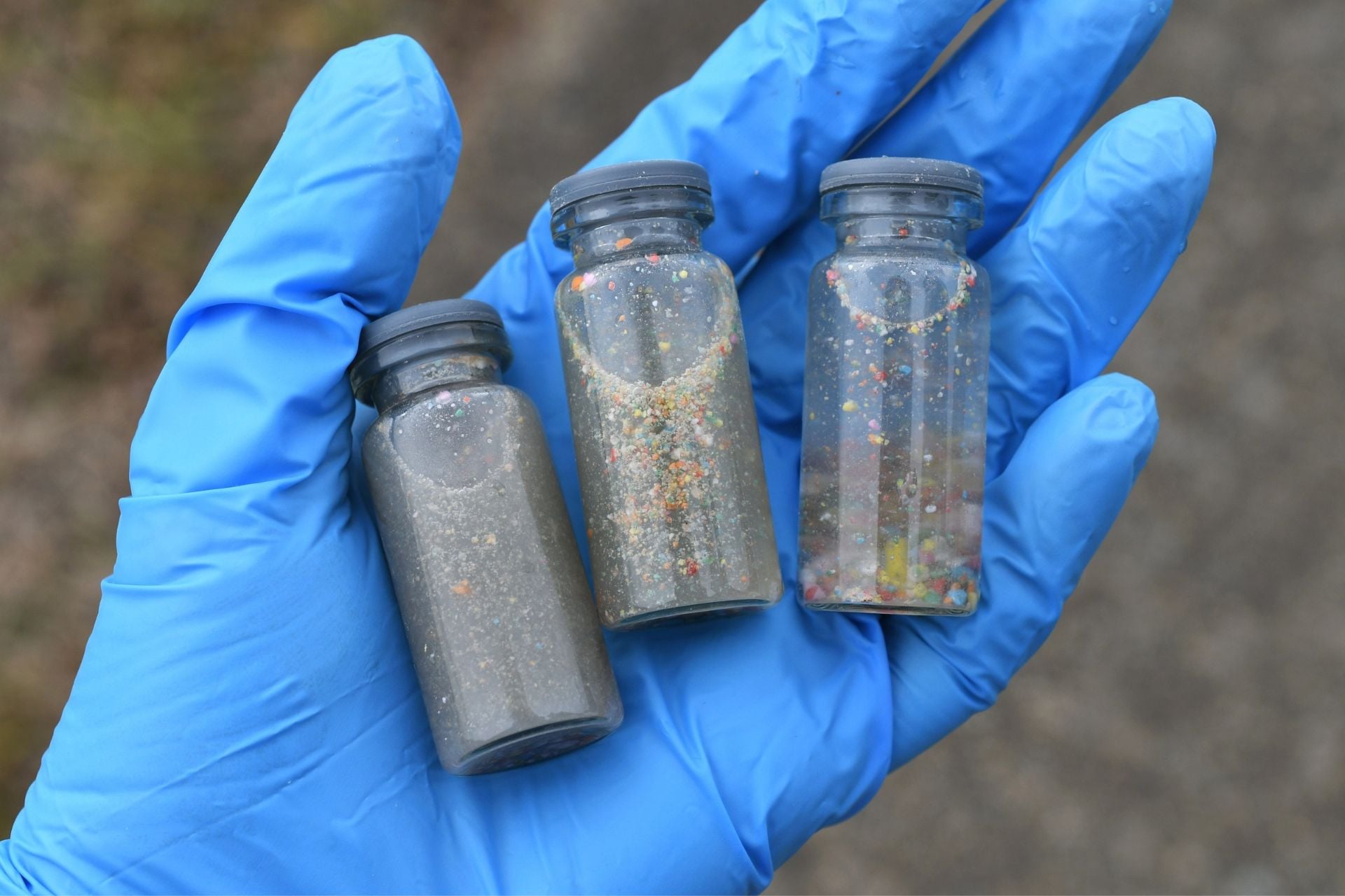 A gloved hand holding vials of water samples to test for pollution and plastic contamination.