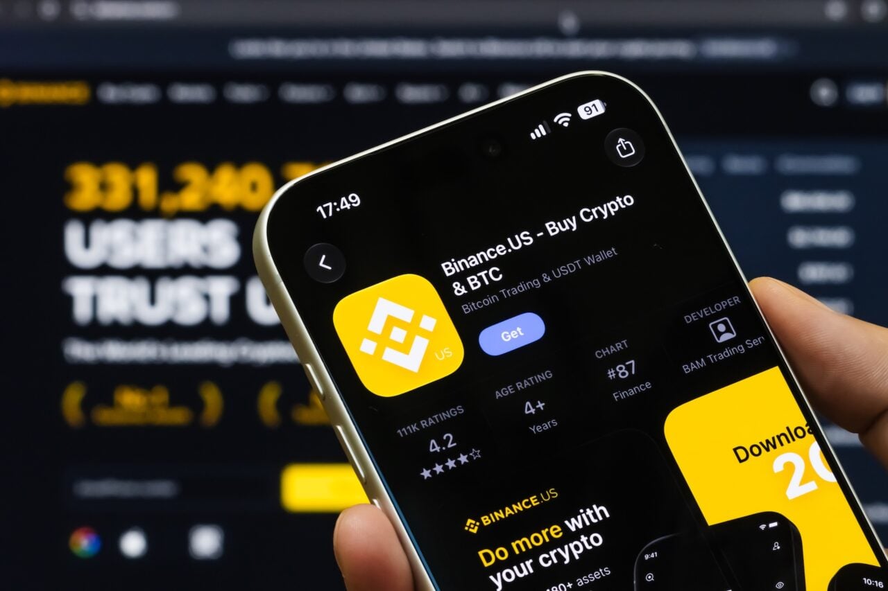 In this photo illustration, a hand holds a smartphone displaying the App Store listing for Binance.