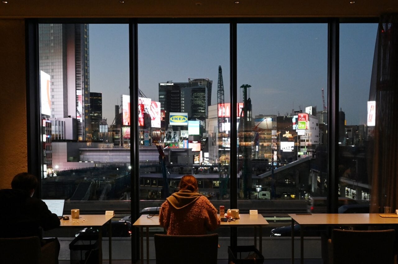 People work in a café with a view of the Shibuya skyline in Tokyo on December 4, 2025.
